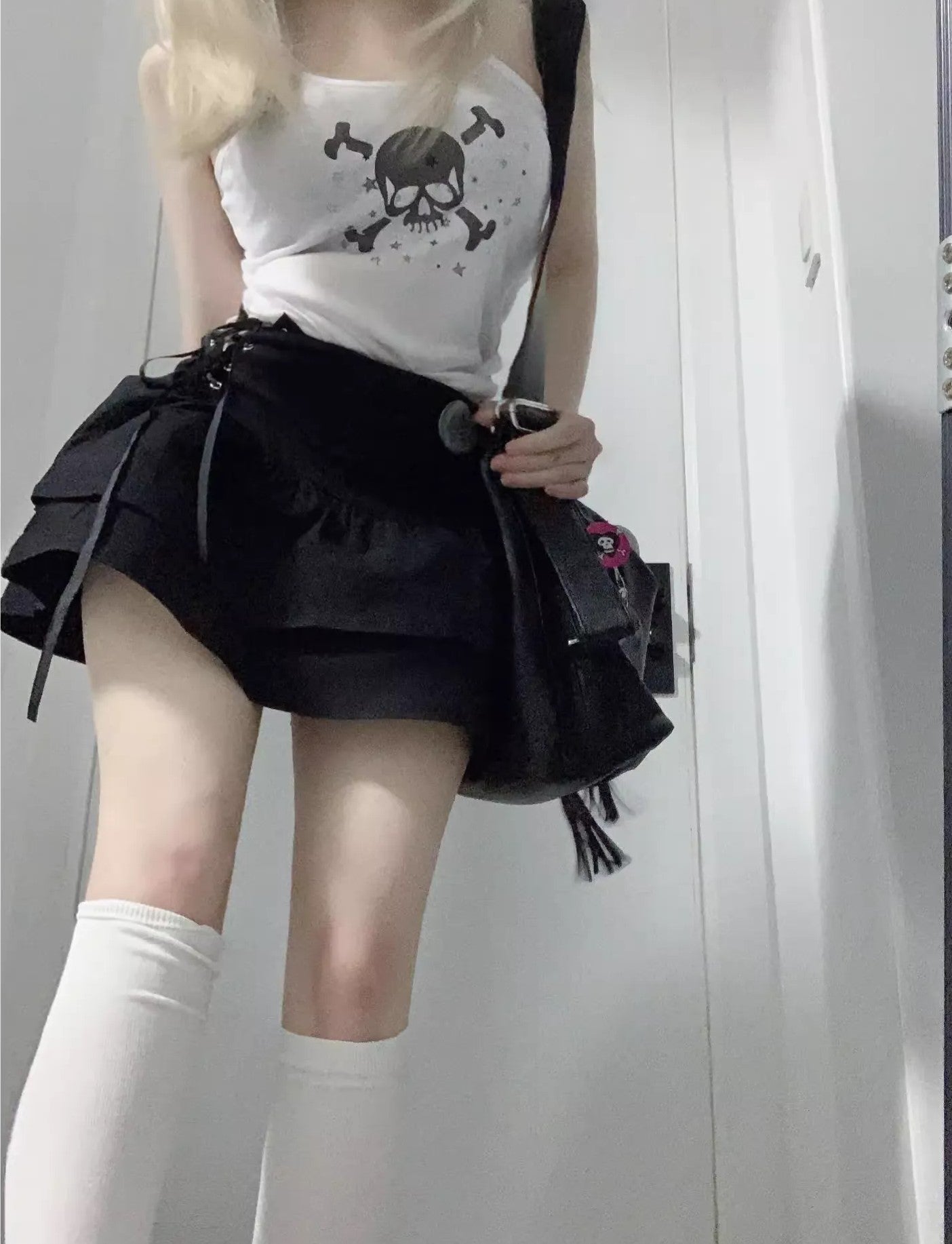 Person wearing a white top with a skull design and a black skirt, standing against a plain background.