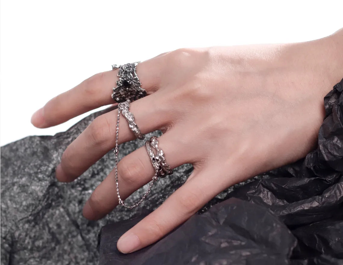 Hand wearing multiple silver rings on a textured surface