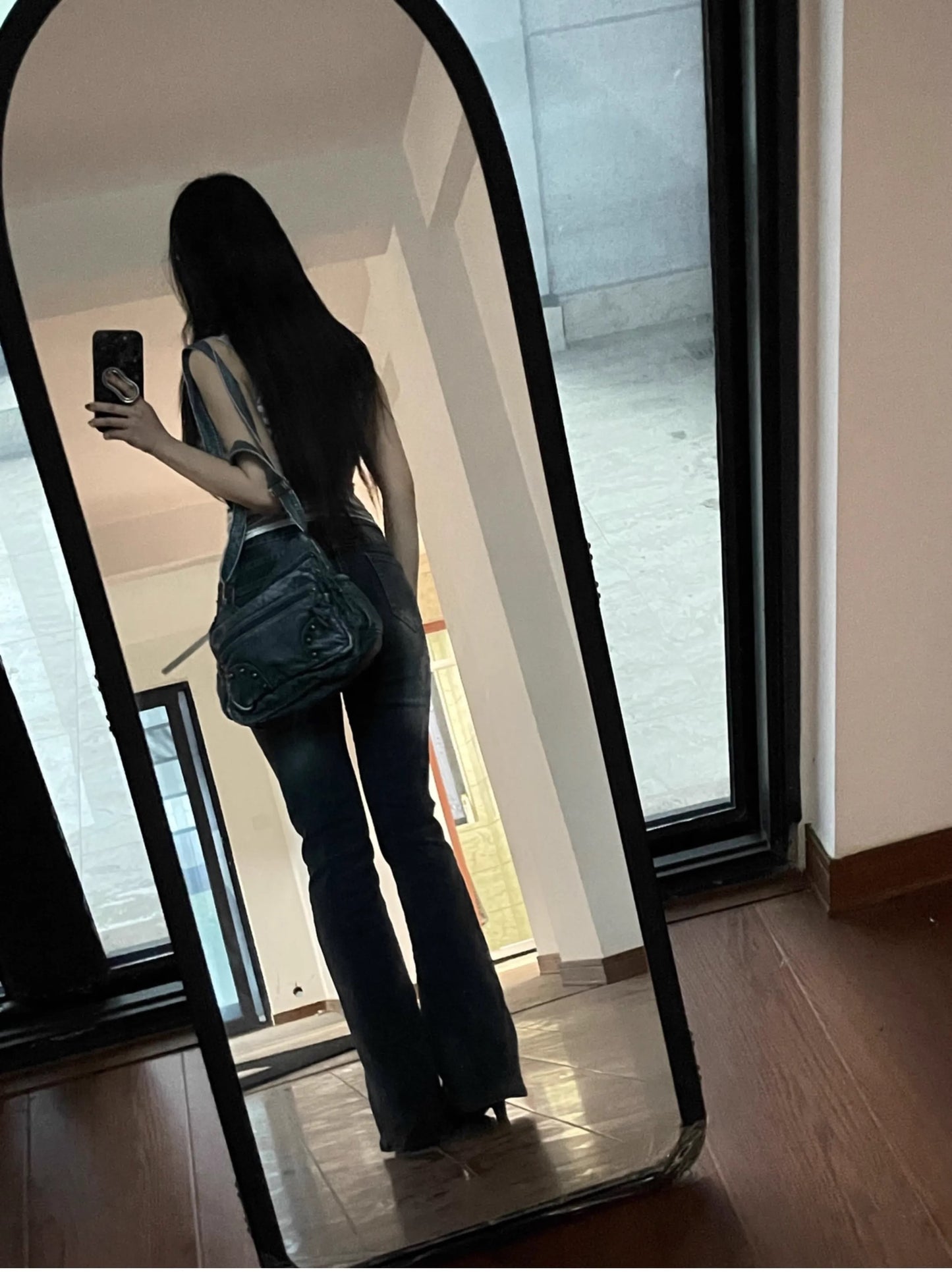 Person taking a mirror selfie wearing a black outfit with a blue bag.