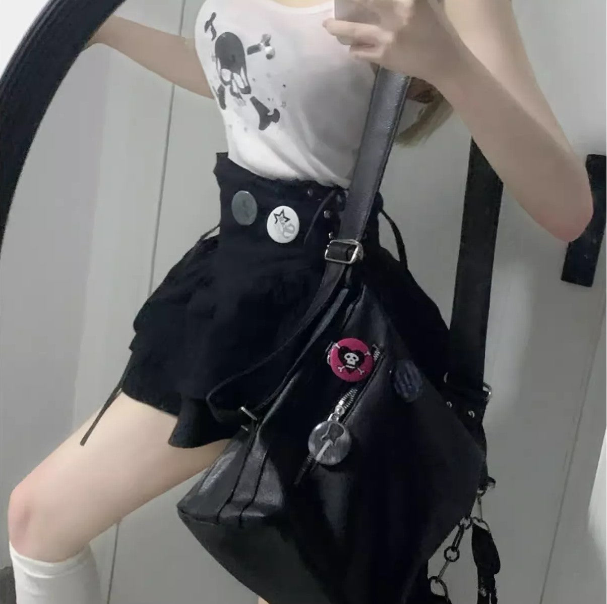 Person wearing a black skirt and white top with skull design, holding a black bag.