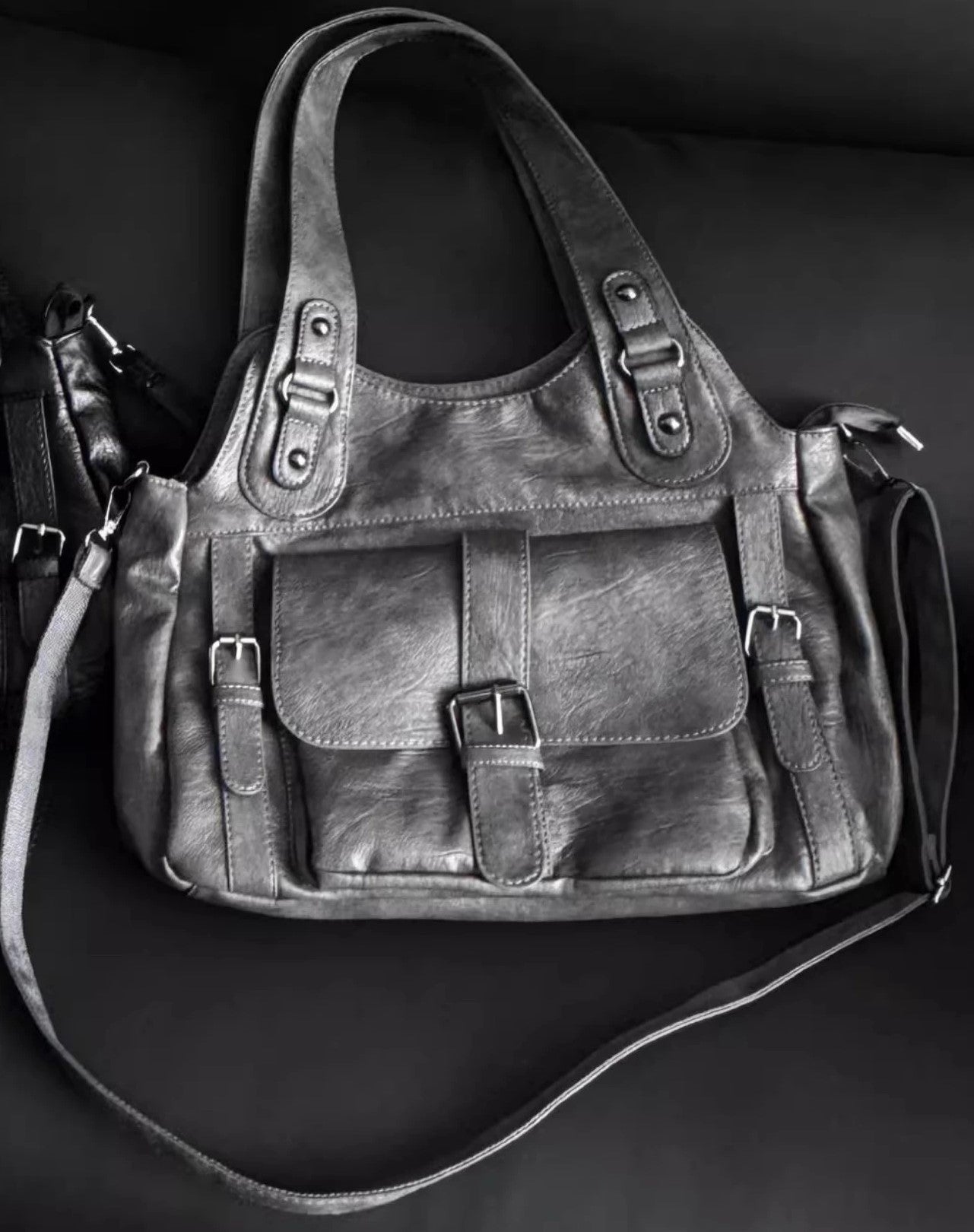 Gray leather handbag with multiple straps on a dark background