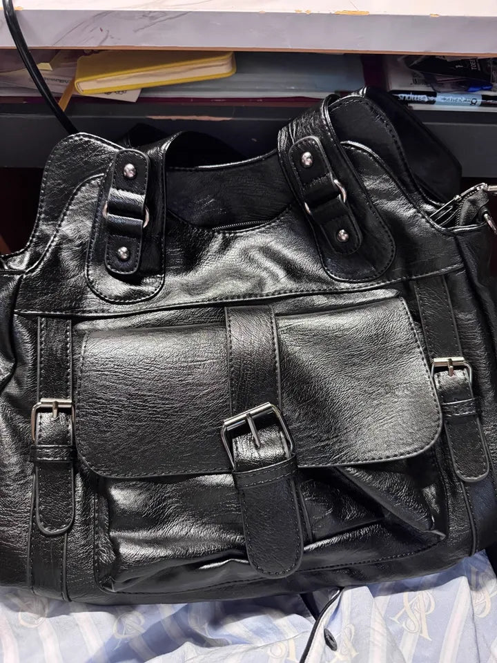 Black leather bag with multiple buckles on a surface
