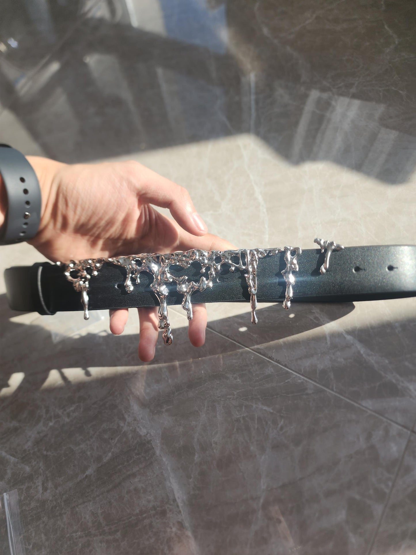 Black belt with silver buckles held by a hand on a reflective surface