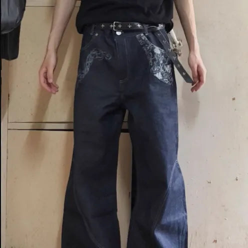 Person wearing dark blue jeans with floral embroidery on a plain background