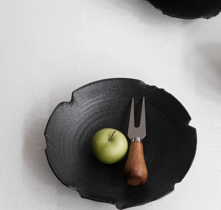 Black stone bowl with a green apple and wooden-handled fork on a white background