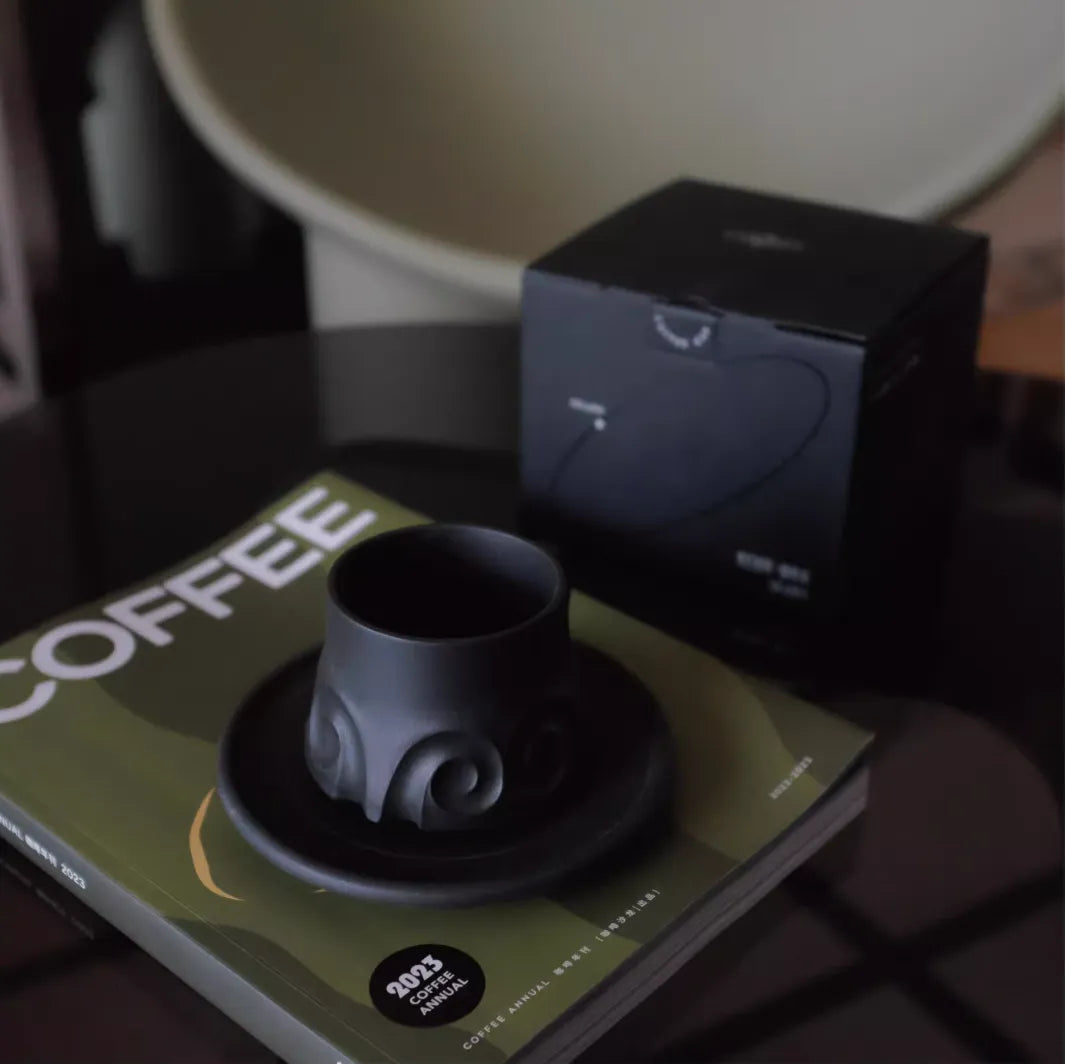 Black ceramic cup and saucer on a book titled 'COFFEE' with a blurred background