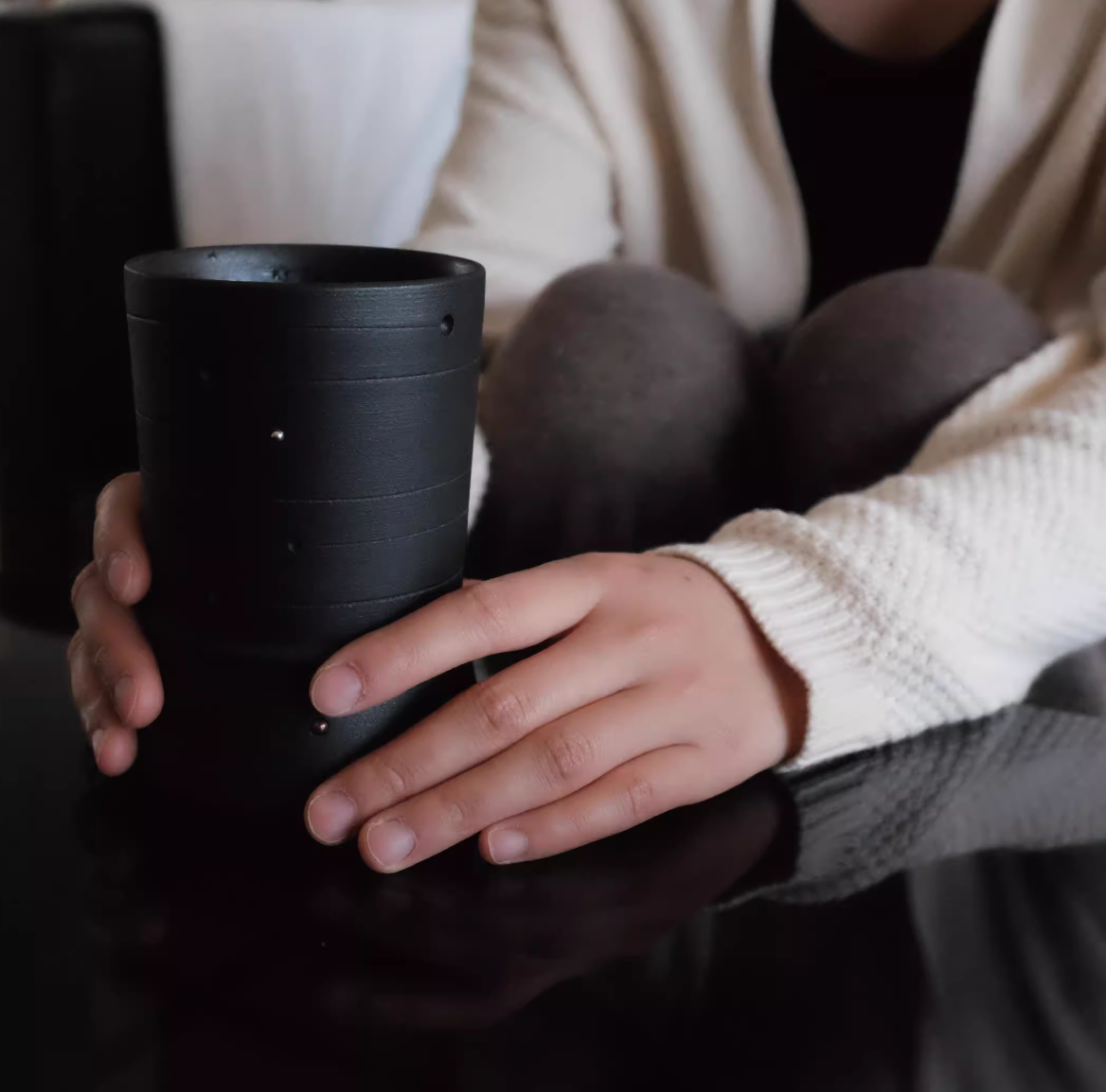Person holding a black cylindrical object on a reflective surface