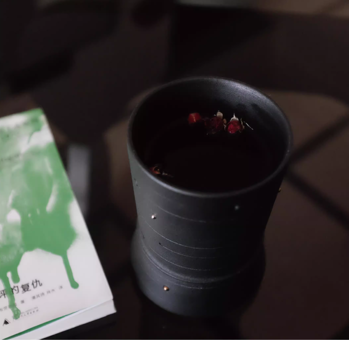 Black ceramic cup with dried flowers on a dark surface next to a green book