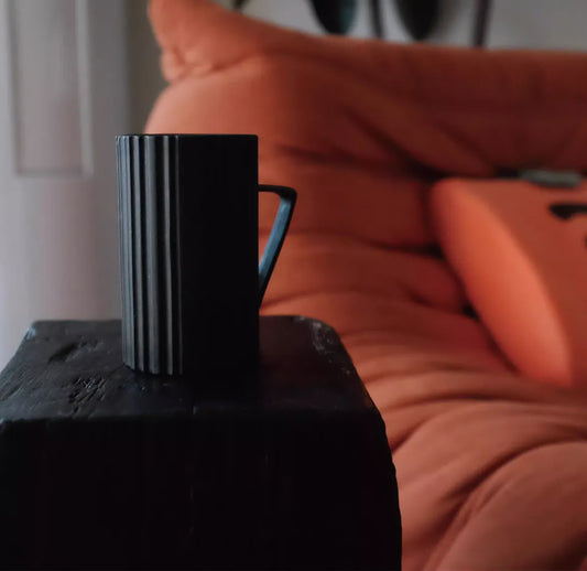 Black mug on a wooden surface with orange cushions in the background