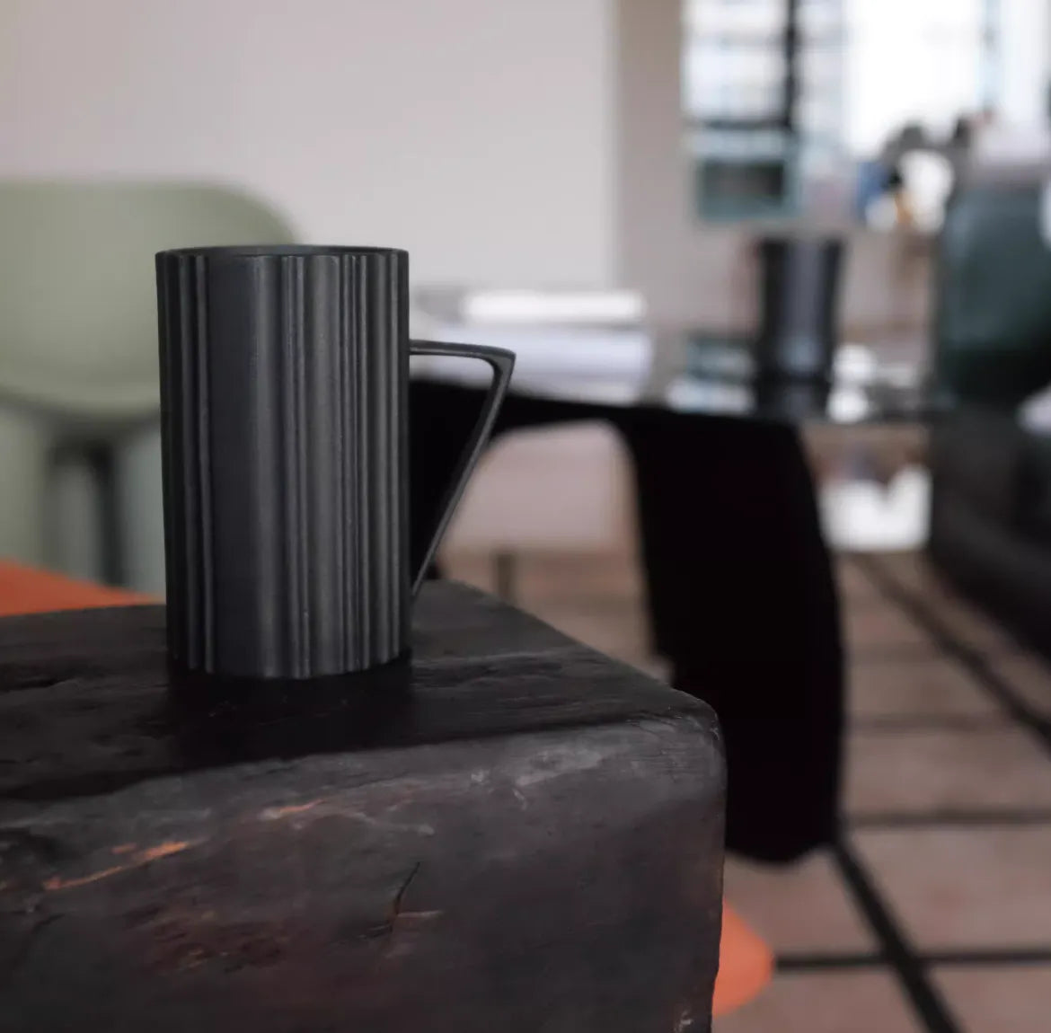Black ceramic pitcher on a wooden surface with a blurred indoor setting