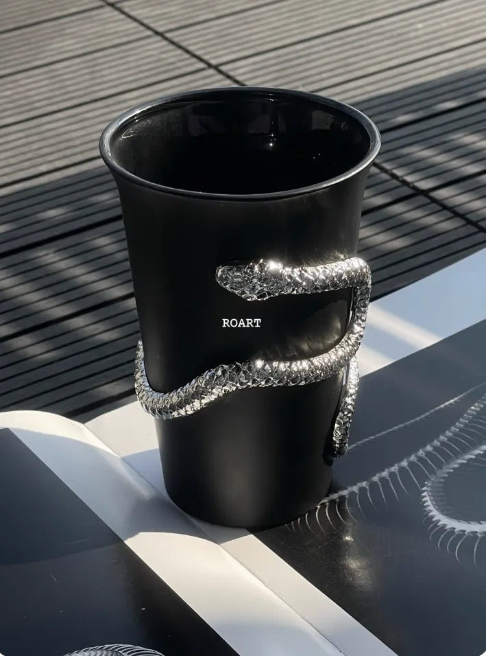 Black cup with decorative silver handle on a wooden surface