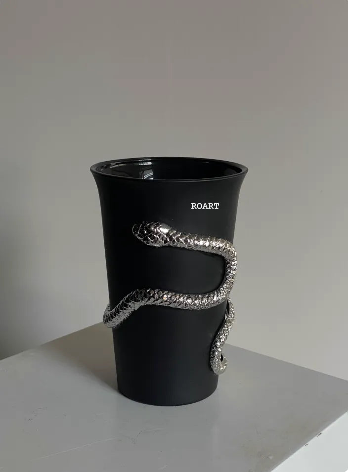 Black cup with a silver snake design on a gray surface