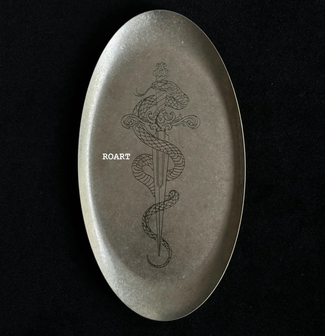 Oval stone with engraved snake and sword design on a black background