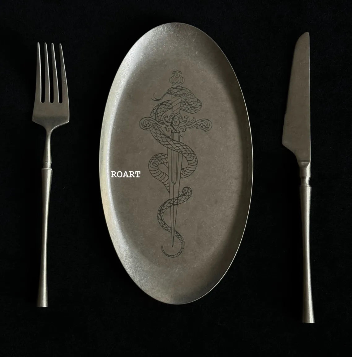 stainless steel plate with snake design and 'ROART' branding, accompanied by a fork and knife on a black background.